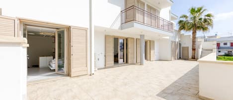 A modern two-story building with a balcony, a palm tree, and a tiled courtyard.