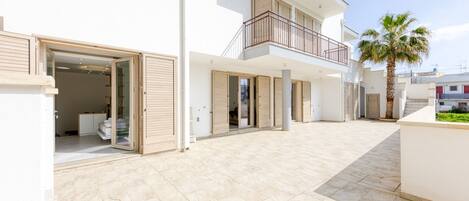 Un edificio moderno de dos pisos con un balcón, una palmera y un patio empedrado.