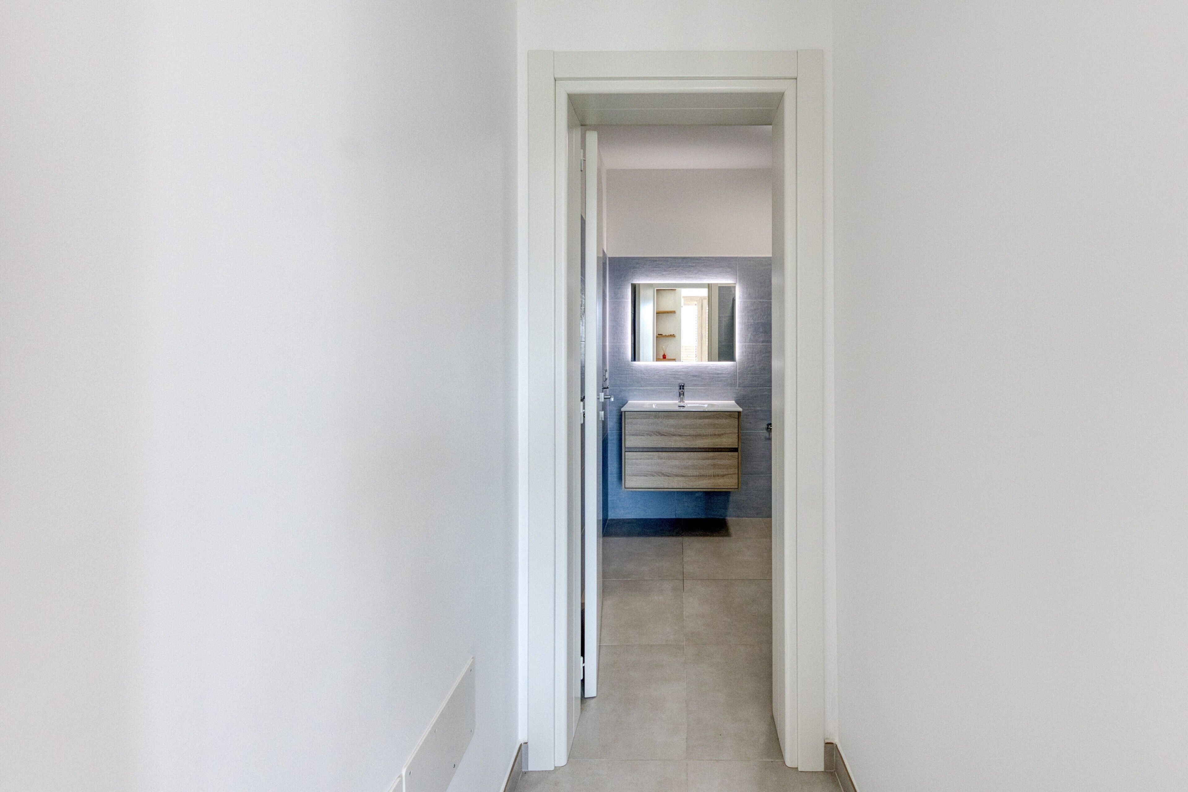 Een smalle gang die leidt naar een badkamer met een ingebouwd wastafel en een spiegel.