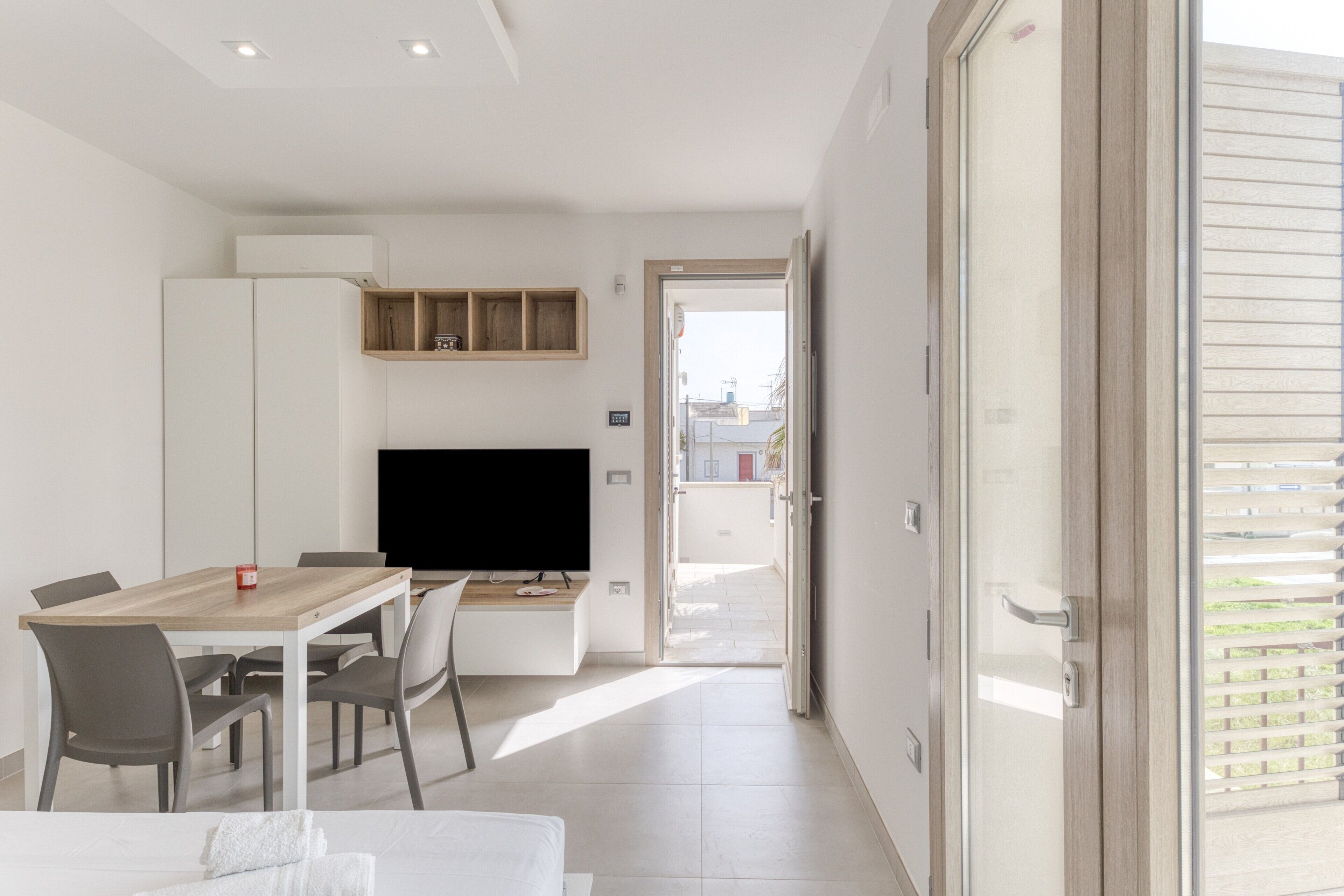 Une chambre d’hôtel moderne dotée d’un coin repas, d’une télévision et d’un balcon avec stores.