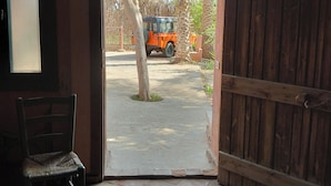 An open doorway leading to a paved area with a parked vehicle, a chair, and a wooden fence.