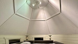 Een slaapkamer met een schuin dak, een bed met een sprei met geometrische patronen, twee nachtkastjes met lampen, en een kleine open haard.