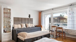 A bedroom with a bed, a desk, a chair, a radiator, and a window with curtains. - Schönwald Black Forest Homes – Apartment with Pool, Small Lake, 100 m to Ski Lift (Schönwald im Schwarzwald)