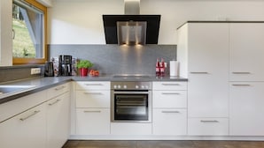 Una cucina moderna con forno integrato, elettrodomestici in acciaio inossidabile, mobili bianchi e una finestra vista verde.