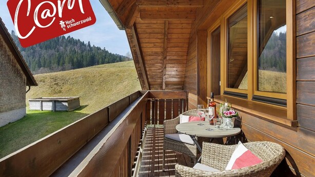 Un balcone in legno con mobili in vimini, un tavolo con bevande e una vista panoramica su un prato.