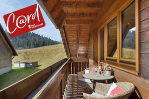 Een houten balkon met rieten meubilair, een tafel met drankjes en een prachtig uitzicht over een grasveld.