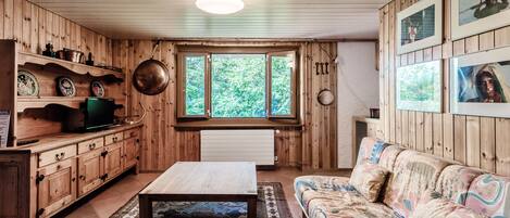A wooden interior with a sofa, a coffee table, a television, and a window with a view of greenery.