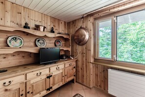 Un interior de fusta amb televisió sobre un moble, plats decoratius i una finestra gran amb vistes a vegetació.