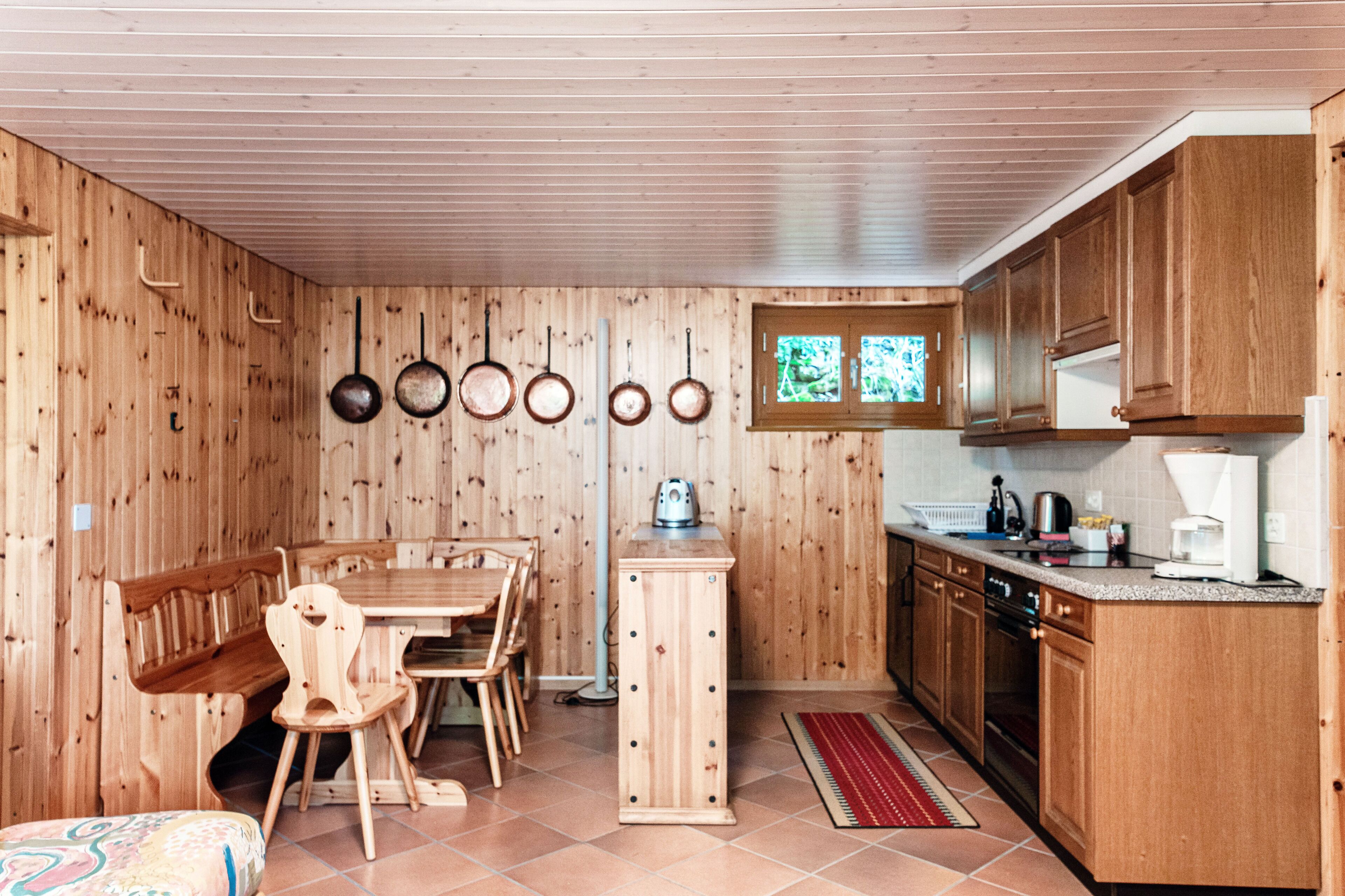 A wooden interior with a dining table, chairs, a kitchen with cabinets, and hanging pots.