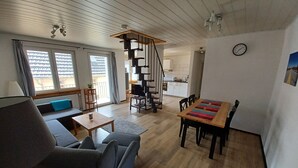 Una sala de estar moderna con un sofá, una mesa de centro, una mesa de comedor con sillas, una escalera y una cocina al fondo.