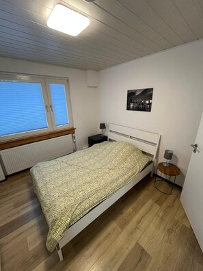 A bedroom with a bed, a nightstand, a lamp, a picture on the wall, and a window with blinds.