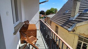 Un balcón con una mesa y sillas de madera, barandilla de metal y vistas a edificios vecinos.