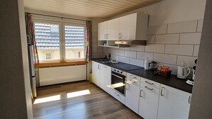 Una cocina con armarios blancos, encimera negra y ventana con cortinas.