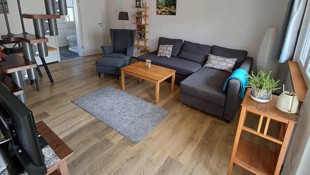 Una sala de estar moderna con un sofá gris, una mesa de centro de madera y una escalera con barandilla de madera.