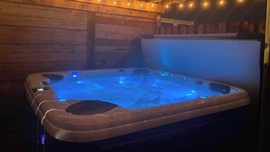 A hot tub with blue LED lights in a wooden cabin with string lights on the ceiling. - Family-Friendly 3BR, HotTub, Patio, Bar, Fireplace (Paradise)