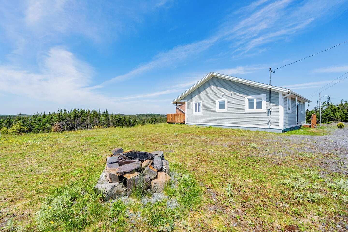 A single-story house with a sloped roof, a front porch, and a stone fire pit in the yard.