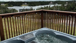 Ein Whirlpool auf einer Holzterrasse mit Blick auf einen See und Häuser in der Ferne.