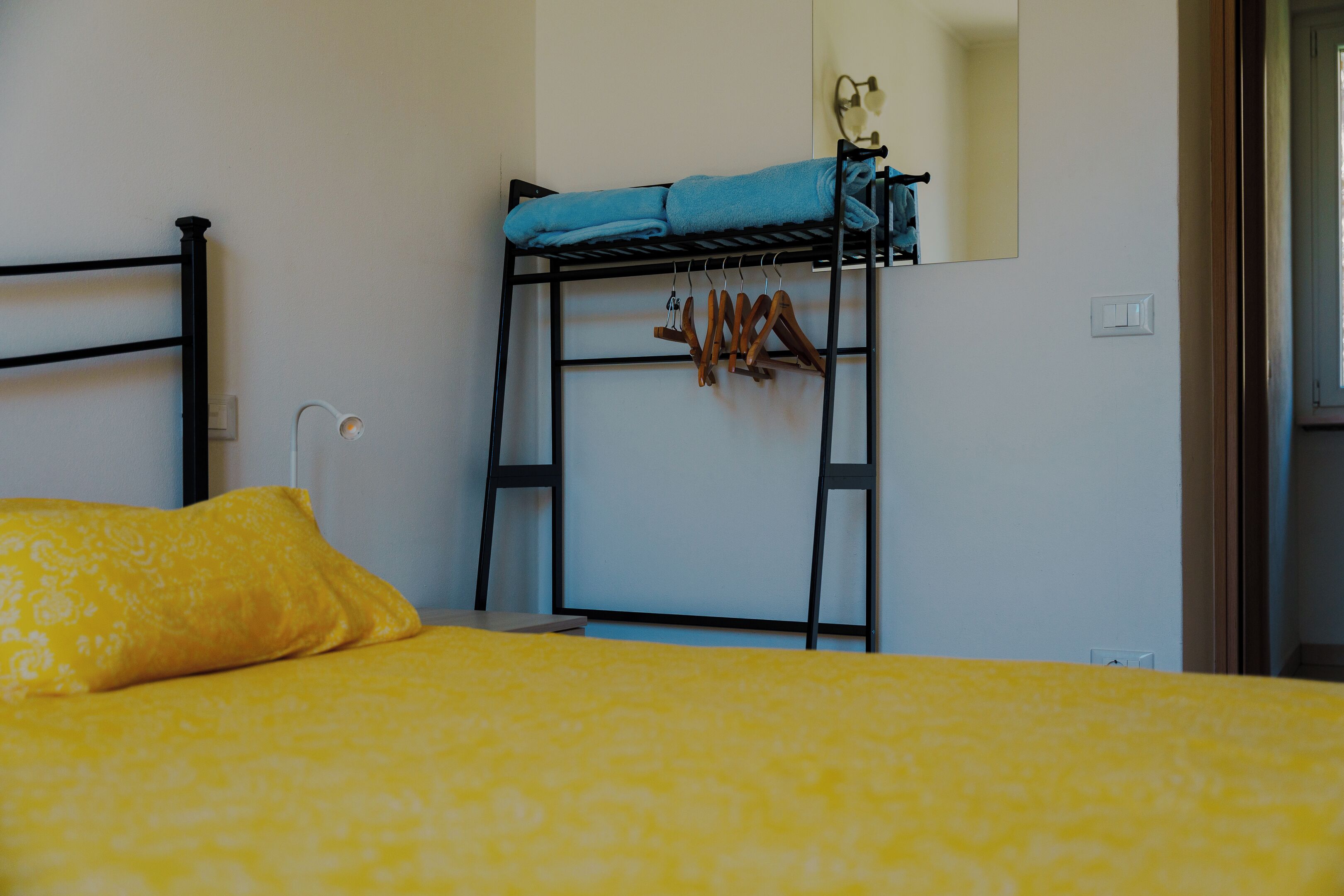 Un lit superposé avec une serviette bleue posée sur le lit du haut, un porte-manteau en bois et une couvre-lit jaune à motifs.