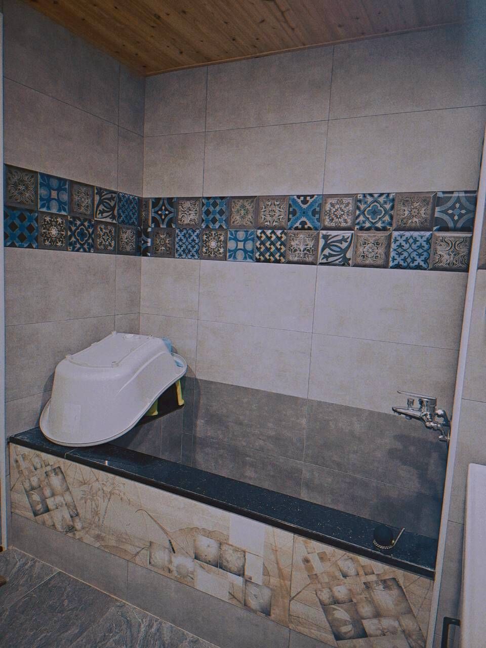 Un baño con bañera, paredes de azulejos y techo de madera.