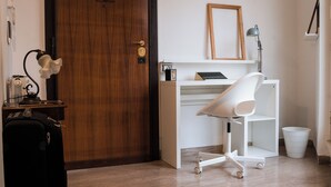 Une pièce avec une porte en bois, un bureau blanc avec une chaise, une lampe et un tableau encadré au mur.