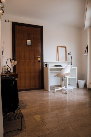 Ein Zimmer mit Holztür, weißem Schreibtisch mit Stuhl, einer Lampe und einem gerahmten Bild an der Wand.