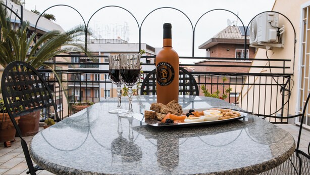 Une table ronde avec une bouteille de vin, des verres et une assiette de collations sur un balcon.