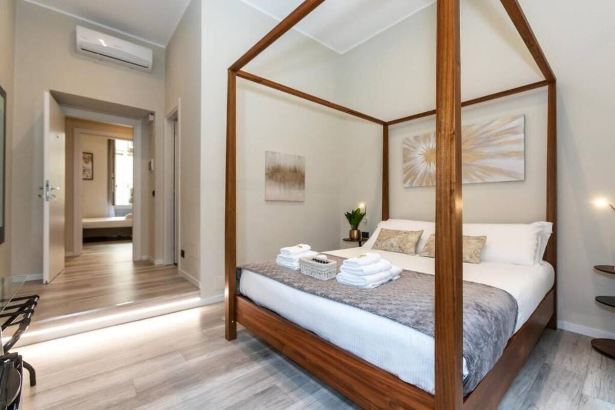 A four-poster bed with a wooden frame, a bedside table with a plant, and a wall-mounted artwork.