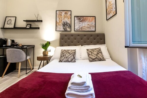 A hotel room with a bed, a desk, a chair, and artwork on the walls. - Suites 44 (Rome)