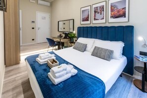 A hotel room with a large bed, a desk, and a chair. There are towels on the bed and a small table with a lamp. - Suites 44 (Rome)
