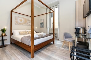 Una cama con dosel de madera, una mesita de noche con lámpara, una silla y un escritorio con asiento.