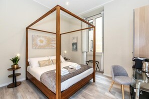 A four-poster bed with a wooden frame, a small bedside table with a plant, a chair, and a desk with a chair. - Suites 44 (Rome)