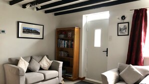 Una sala de estar con un sofá gris, un sillón blanco, una estantería de madera y una puerta con cortina roja.