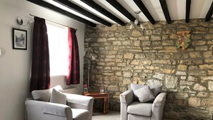 Una habitación acogedora con dos sillones grises, una mesa de madera, un muro de piedra y un ventilador de techo.