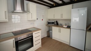 Una cocina moderna con armarios blancos, una campana extractora de acero inoxidable, un microondas integrado y un refrigerador blanco.