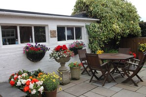 Eine Terrasse mit Tisch und Stühlen, umgeben von Blumentöpfen und Blumen.