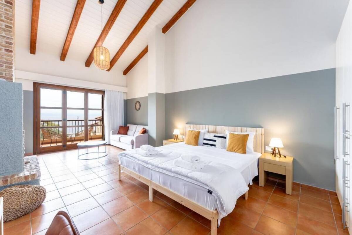 A bedroom with a large bed, a nightstand, a chair, and a view of the outdoors through a sliding door.