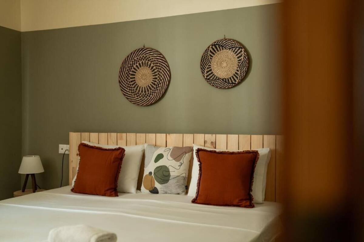 A hotel room with a wooden headboard, a bed with white linens, and two woven wall art pieces.