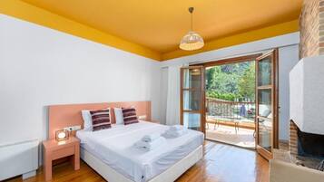 A bedroom with a large bed, a nightstand, a hanging light, and a balcony with a view of greenery.