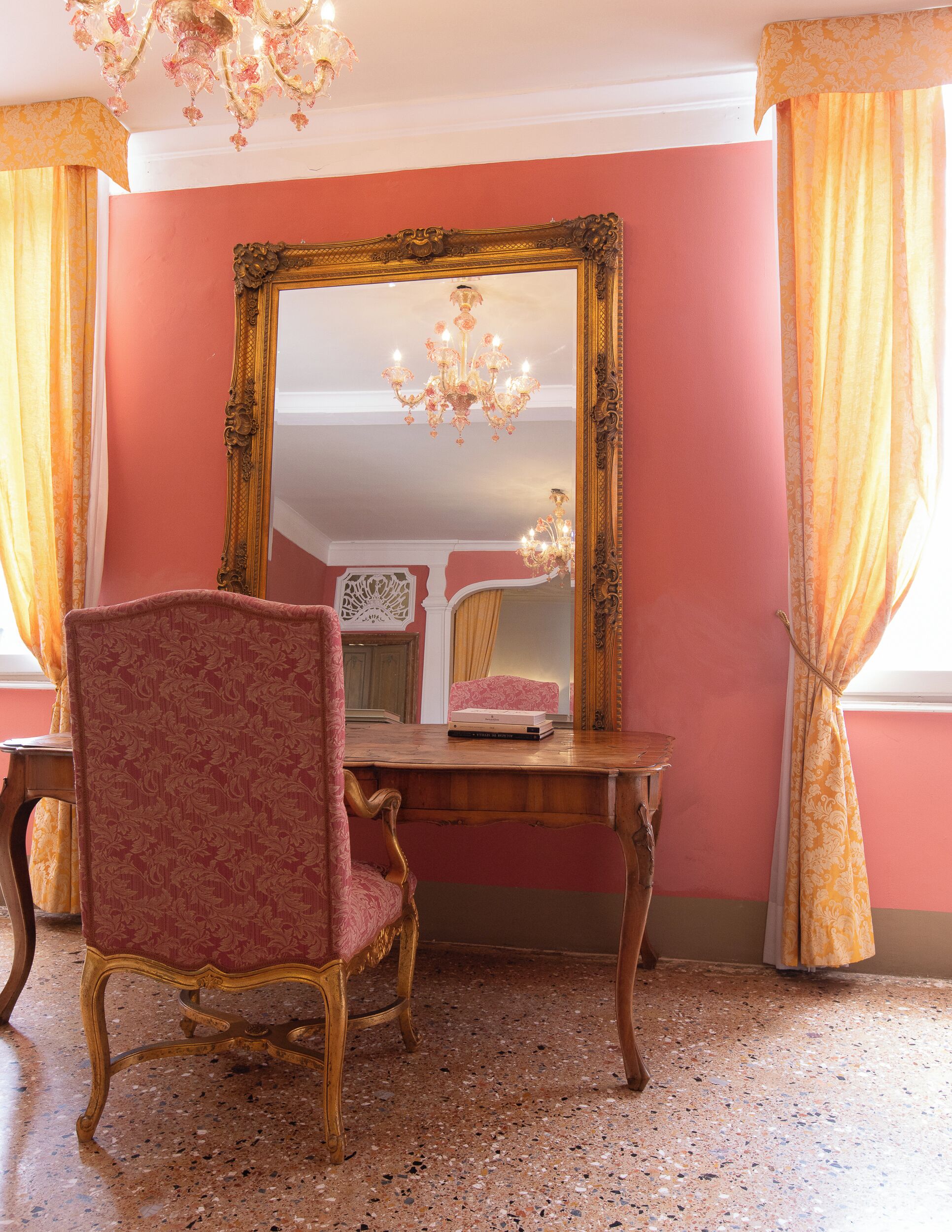 A room with a large ornate mirror, a wooden desk, and a red upholstered chair.