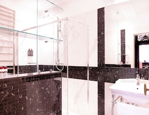 Ein modernes Badezimmer mit einer Duschkabine aus Glas, einem weißen Waschbecken und schwarz-weißen Marmorfliesen.