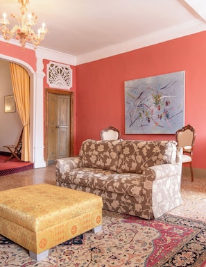 Ein Zimmer mit einer blumigen Couch, einem gemusterten Hocker, einem großen abstrakten Gemälde und einem Chandelier.