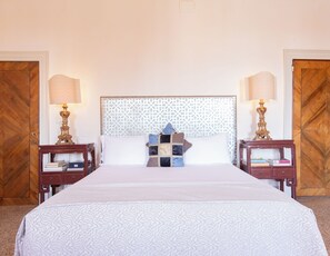 Un lit bien fait, recouvert d’une couvre-lit à motifs, deux tables de chevet avec des lampes et une tête de lit ornée d’un motif géométrique.