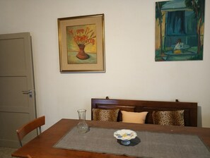 A dining area with a wooden table, a vase, and a bowl on a placemat. There are two paintings on the wall.
