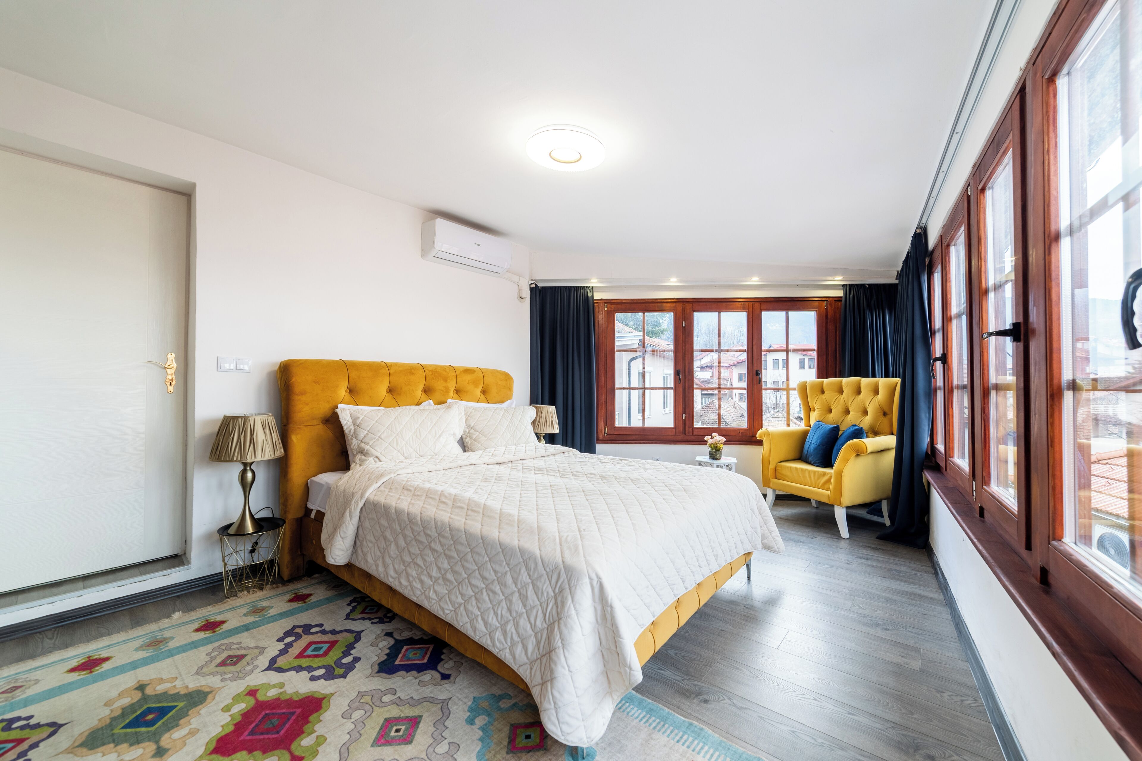 A bedroom with a large bed, a yellow armchair, and a window with curtains.