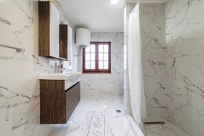 Un baño con piso de mármol, tocador de madera, lavamanos blanco y ventana con vistas.