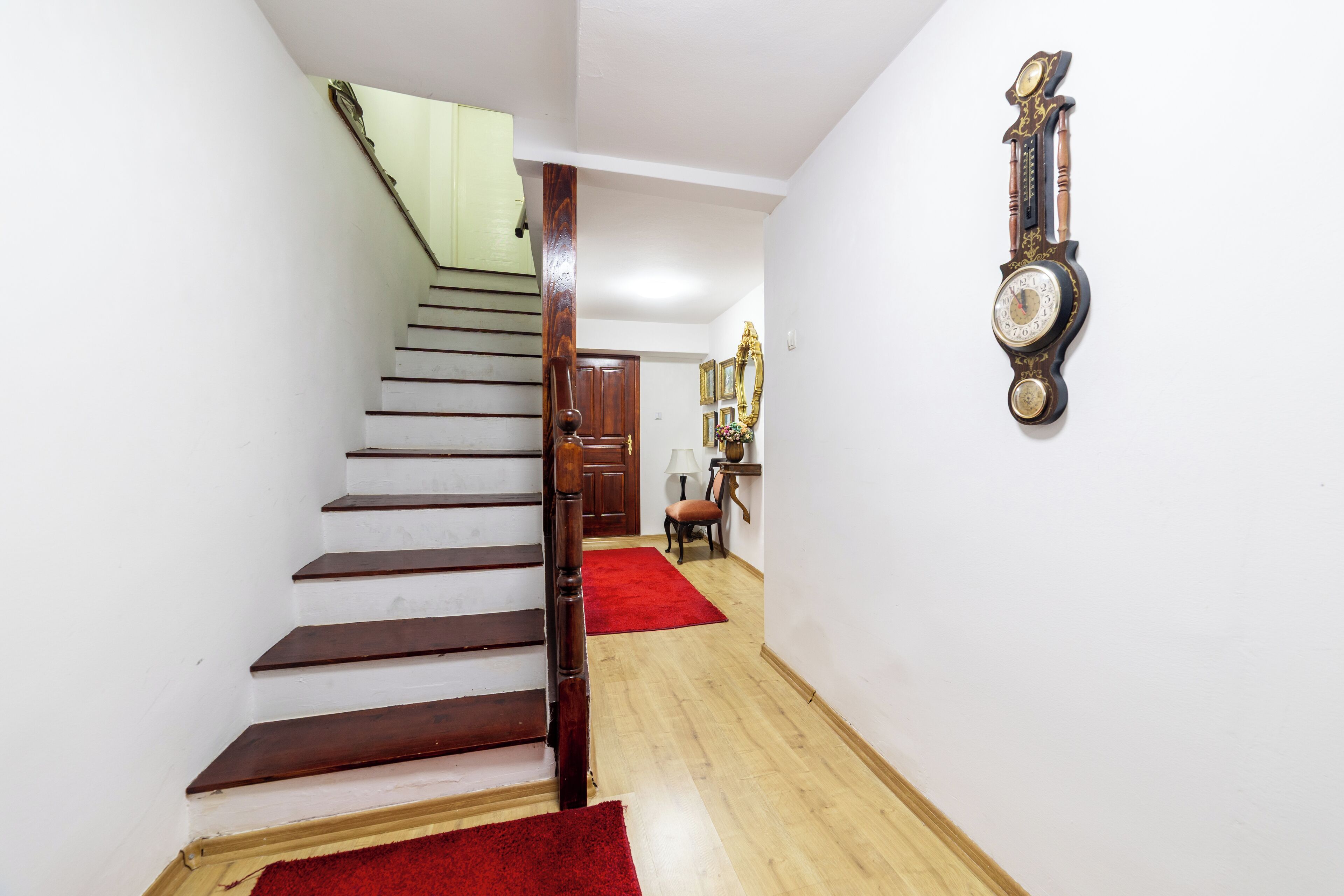 A staircase with wooden steps and a red carpet, leading to a room with a wooden door and a wall-mounted clock.
