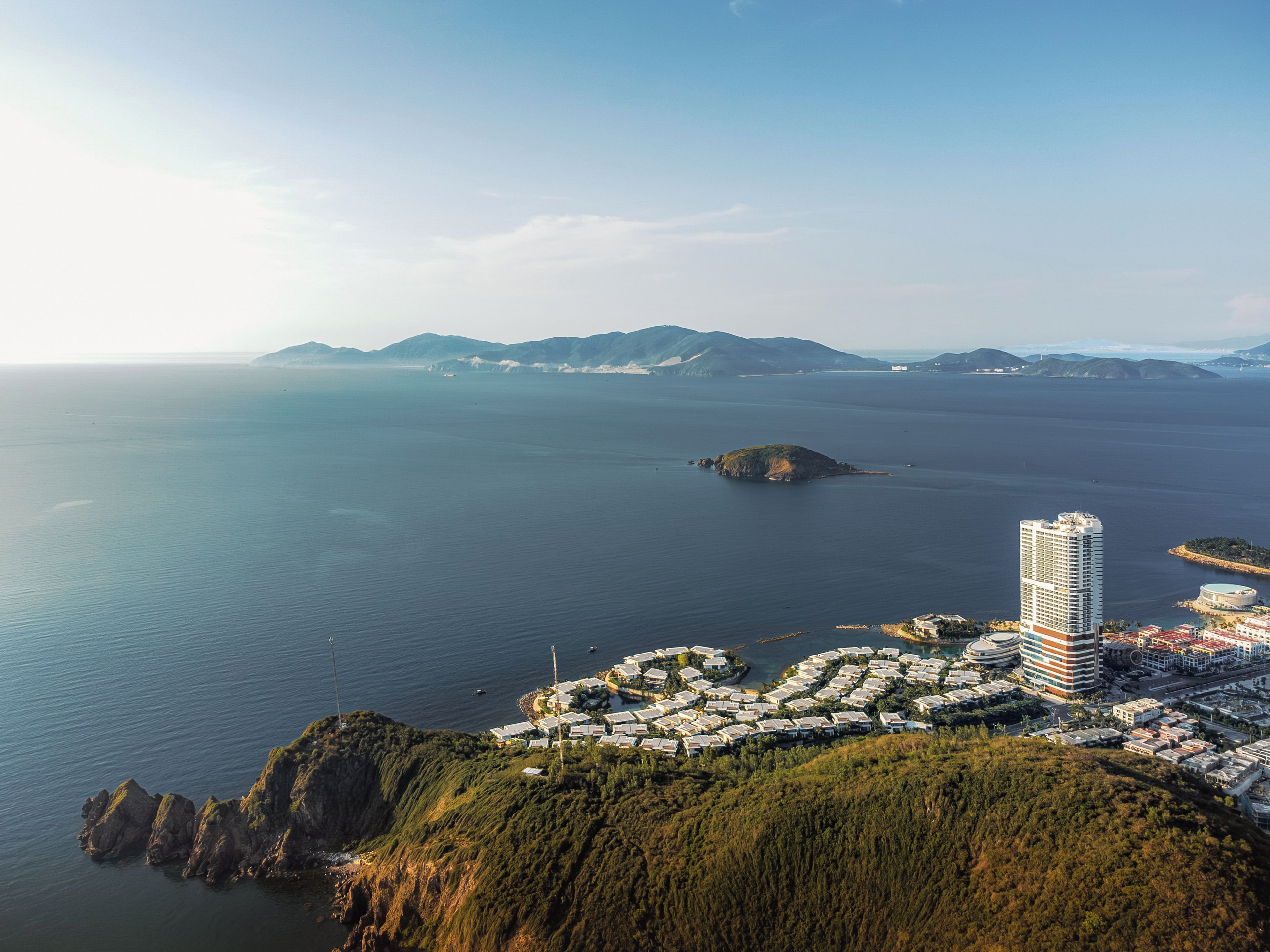 A coastal cityscape with a prominent high-rise hotel, a marina, and a residential area with a hilly backdrop.
