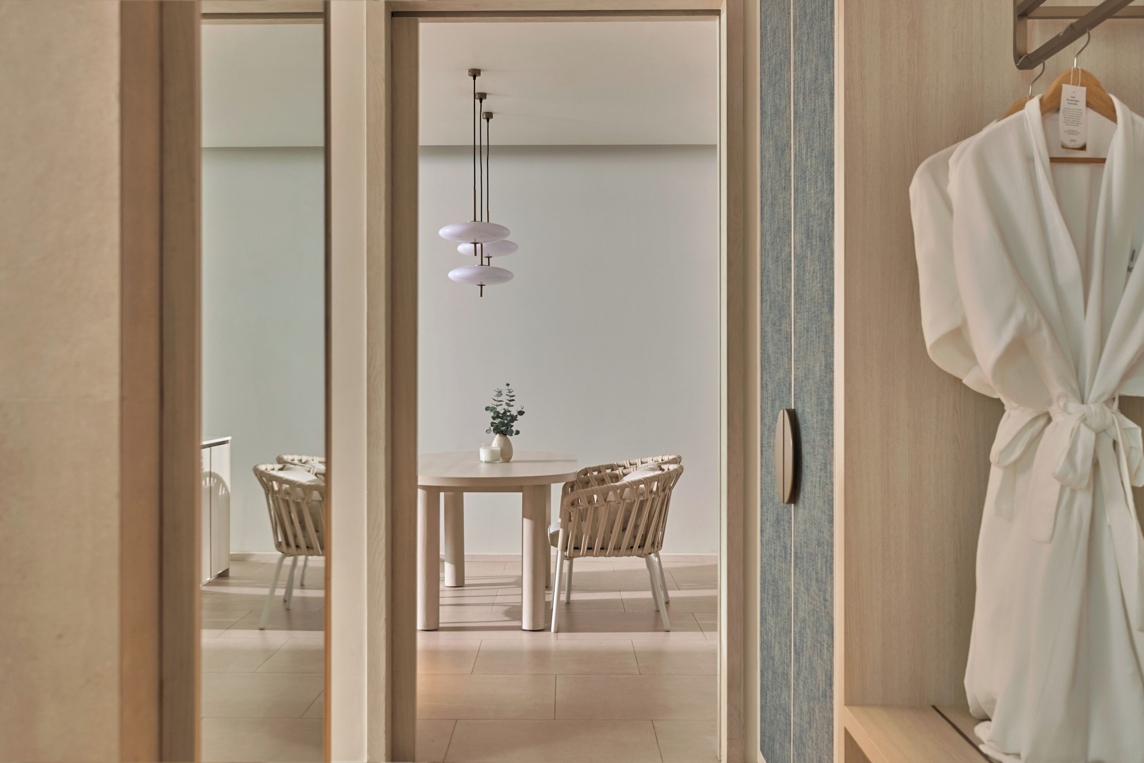 Quarto com uma mesa de jantar, cadeiras, luminária pendente e um roupão em um suporte.