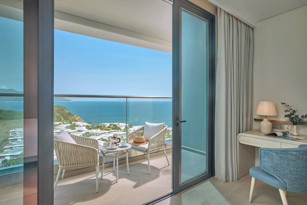 Un balcon avec vue sur la mer, une table avec des chaises, une lampe et une petite plante.