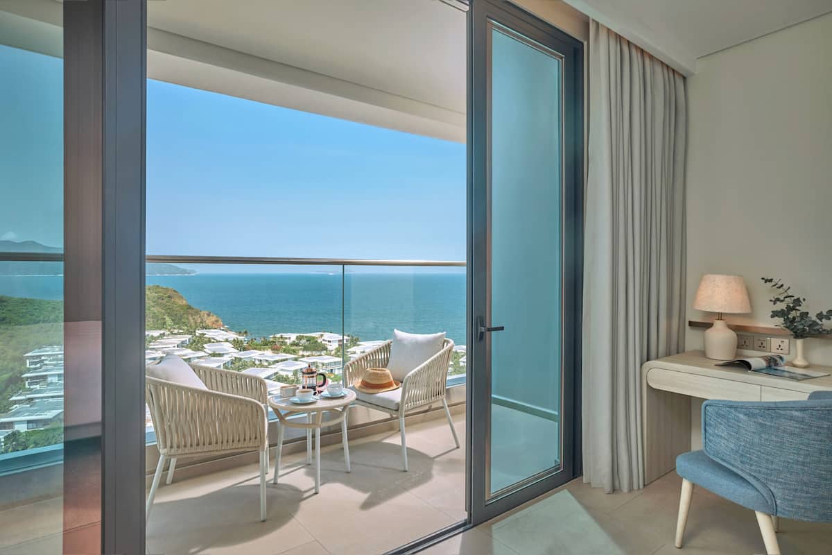 A balcony with a view of the sea, a table with chairs, a lamp, and a small plant.